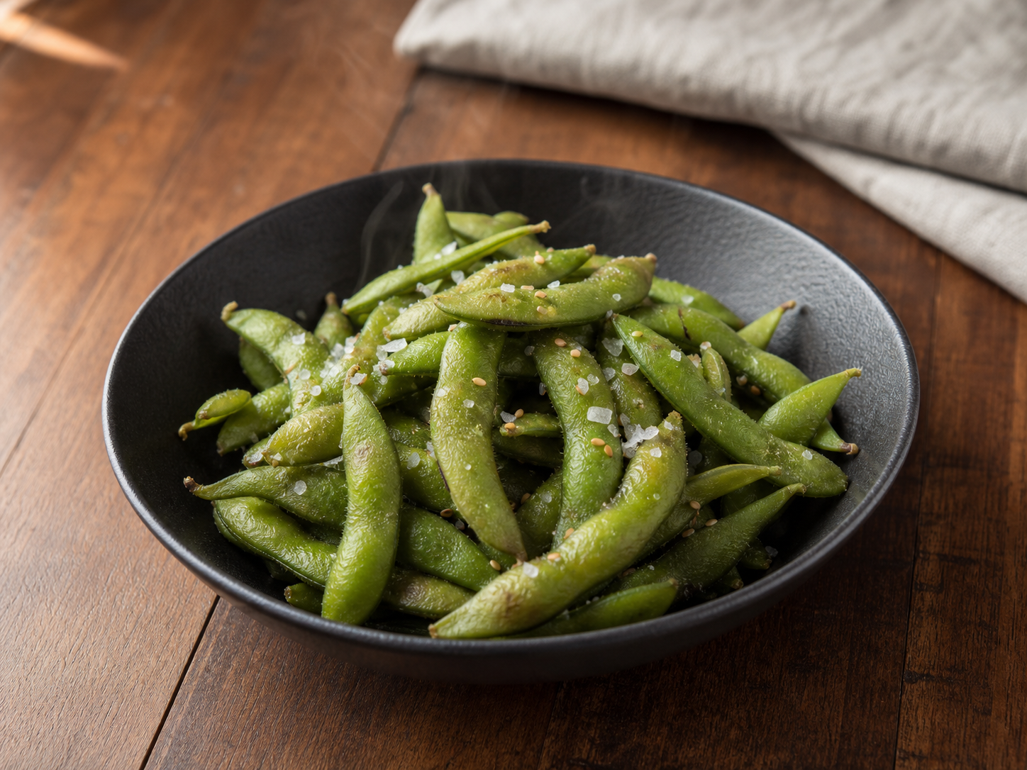 Steamed edamame pods tossed with sea salt and sesame seeds in a black bowl