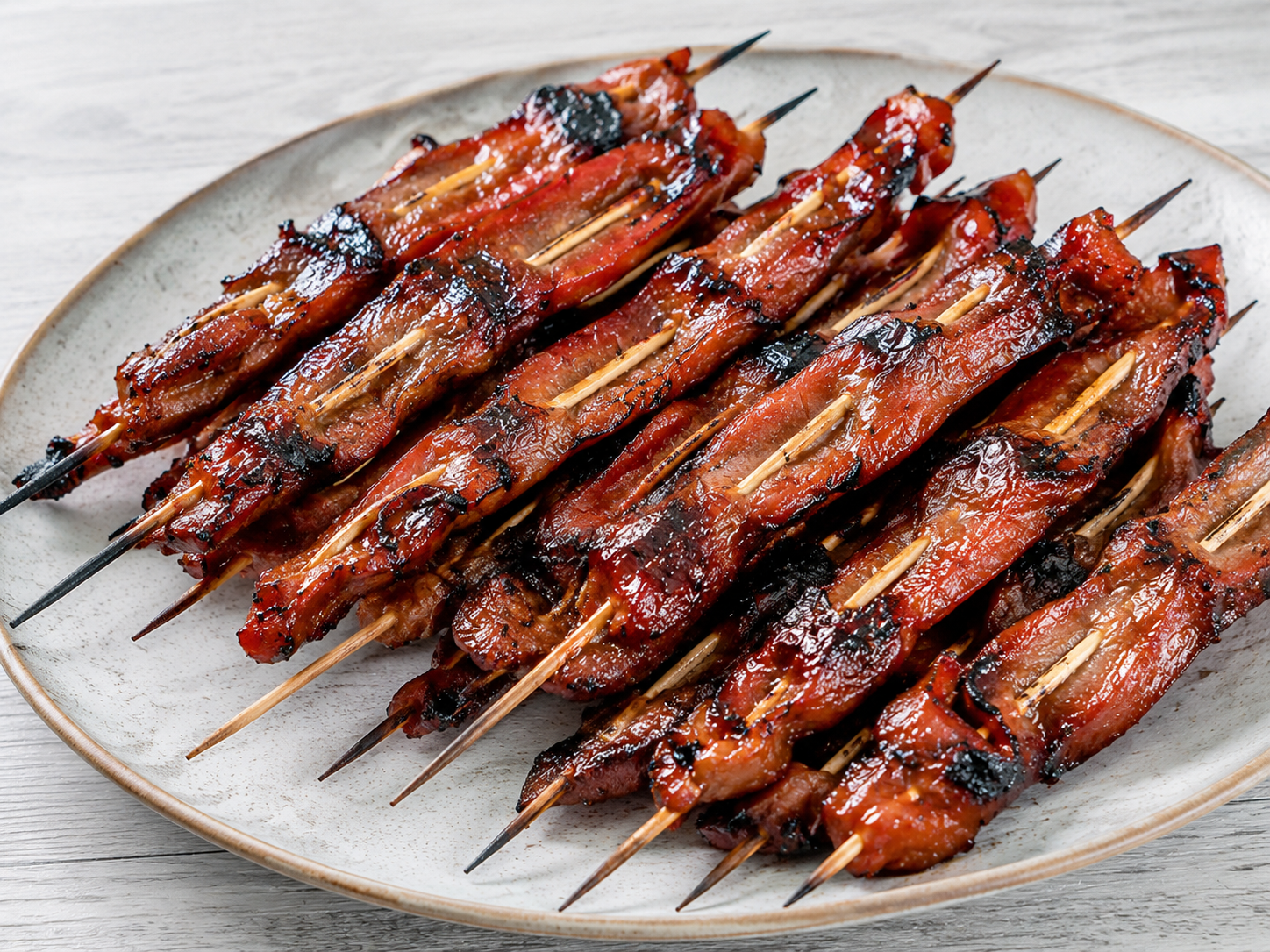 Glossy grilled steak teriyaki strips on wooden skewers with a dark caramelized glaze, sesame seeds and sliced scallions on a white plate