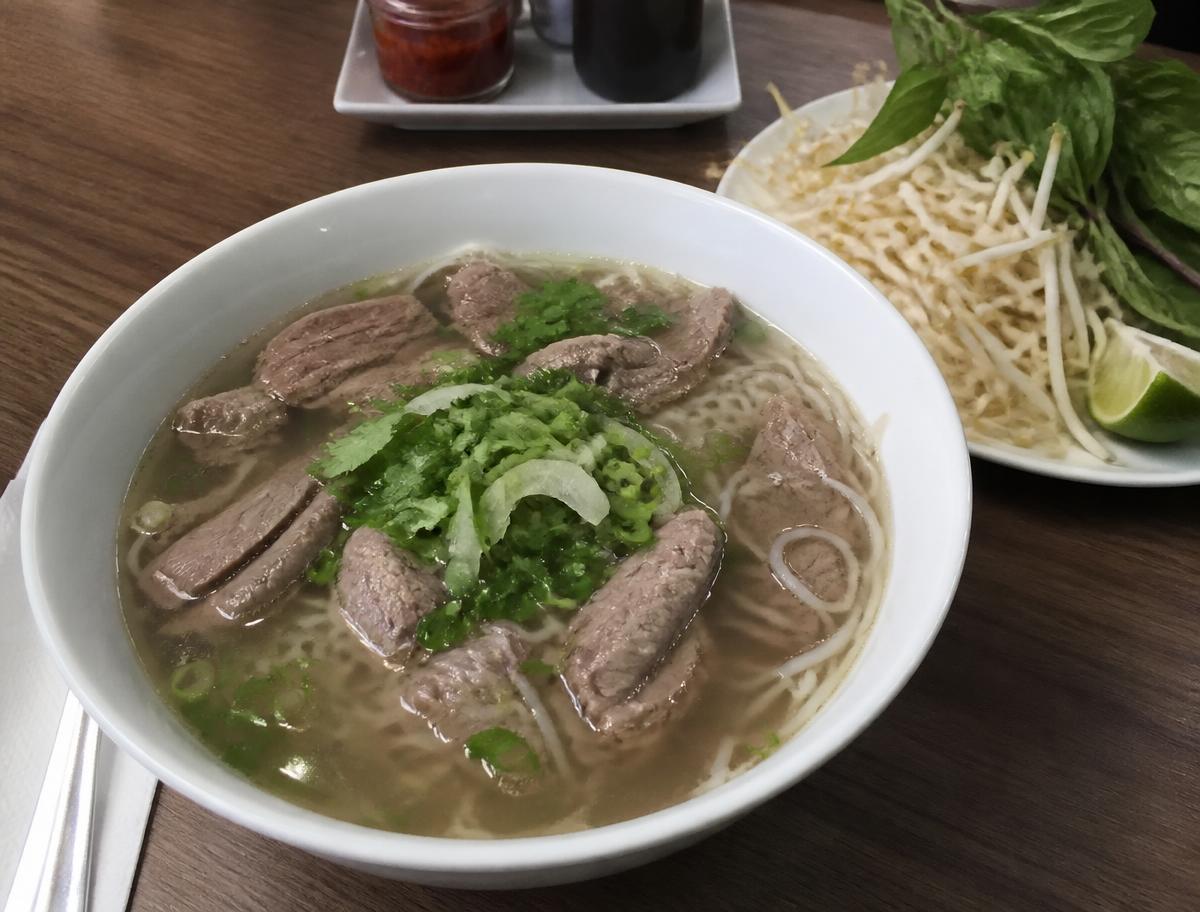 Bowl of Vietnamese brisket pho with clear beef broth, rice noodles, sliced brisket, scallions and cilantro, with bean sprouts, basil and lime on the side