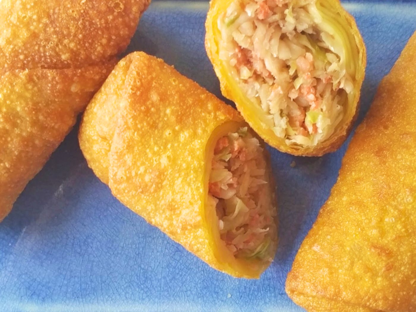 Stack of crisp golden egg rolls on a white plate with a cup of dipping sauce